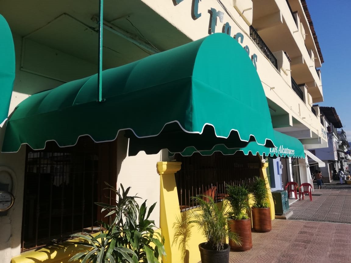 Toldo fijo de medio túnel en lona verde sobre un local comercial